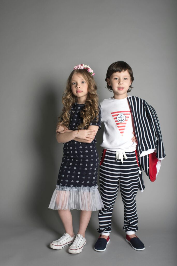 Two children wearing nautical-themed outfits posing confidently in a studio setting.